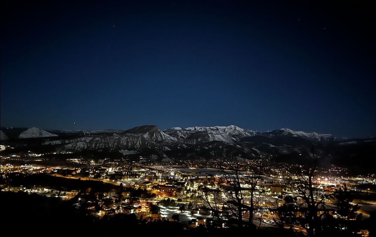 Mountain town glowing beneath snow-covered peaks at night.