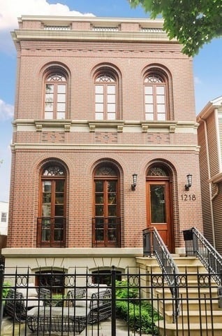 Three-story red brick home with arched windows, a raised front stoop, and fenced patio seating.