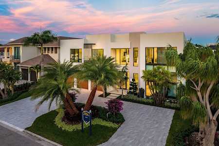Modern two-story home with palm trees, tropical landscaping, and a broad paved driveway at dusk.