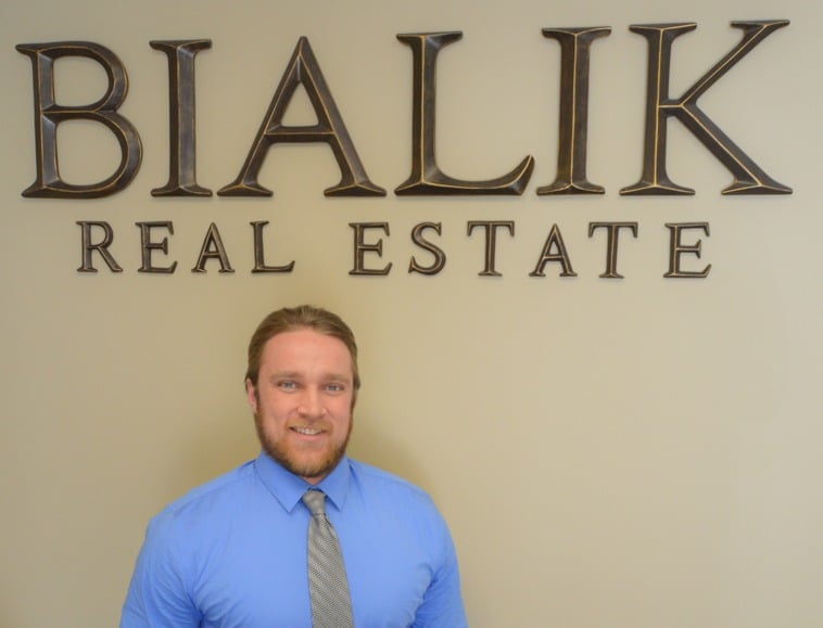 Real estate agent in a blue shirt and patterned tie beneath the Bialik Real Estate sign.