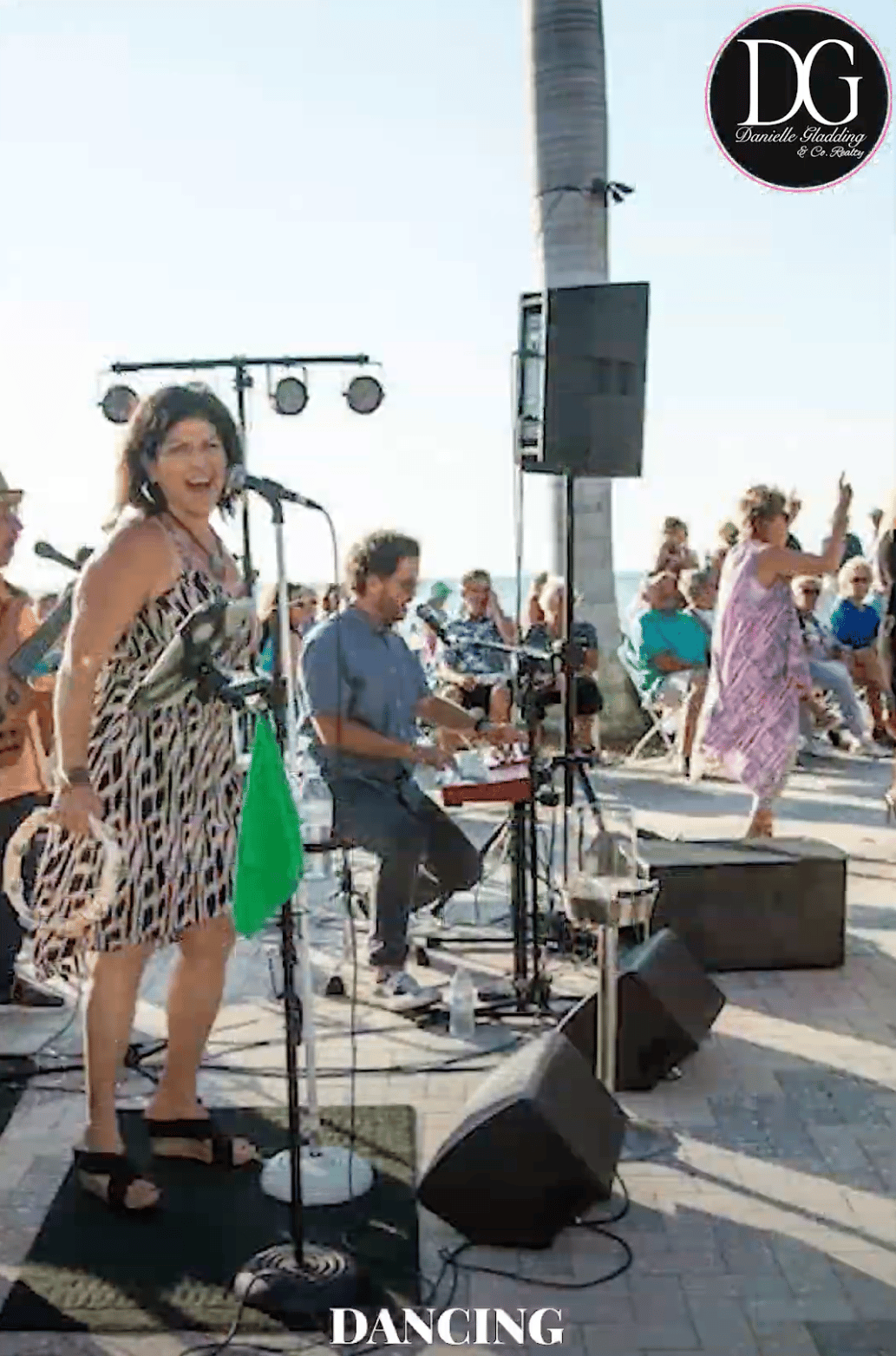 People dance to a live band at an outdoor waterfront event, with spectators seated nearby.