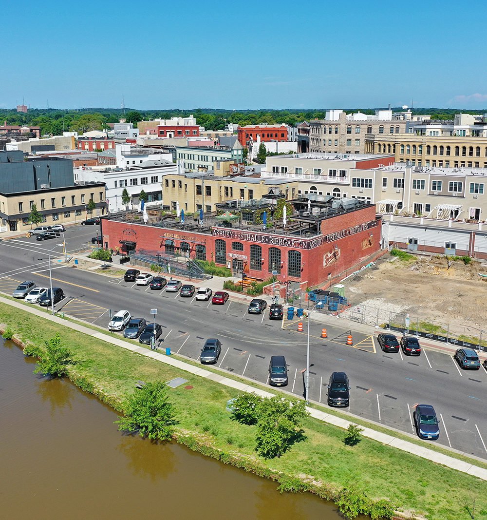 Aerial view of downtown Asbury Park, featuring the red-brick Asbury Festhalle & Biergarten beside a cleared lot.