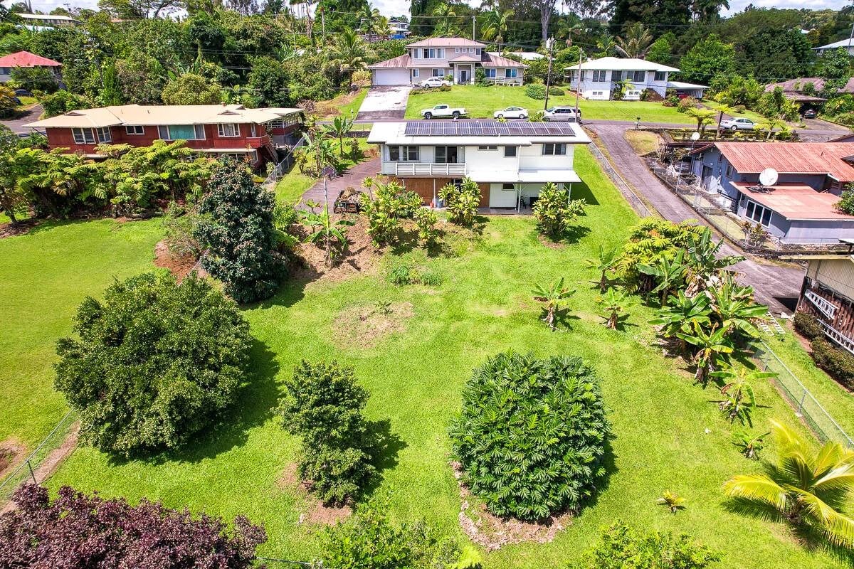 A white two-story Hilo home surrounded by a broad lawn and tropical landscaping.
