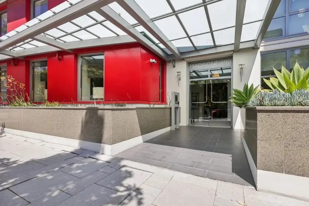Madrone 480 building entrance with red accent walls, glass canopy overhang, modern landscaping, and sleek residential lobby design in San Francisco