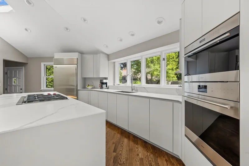 Modern kitchen with a white island, stainless appliances, and windows overlooking trees.