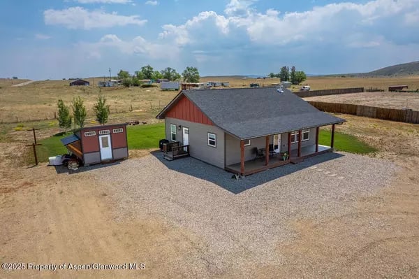 Single-story rural home with a covered porch and detached shed on a gravel lot.