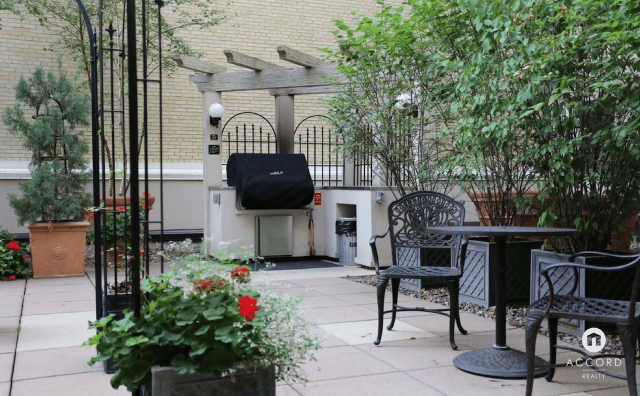 Condo courtyard patio with a pergola, outdoor grill, seating, and leafy planters.