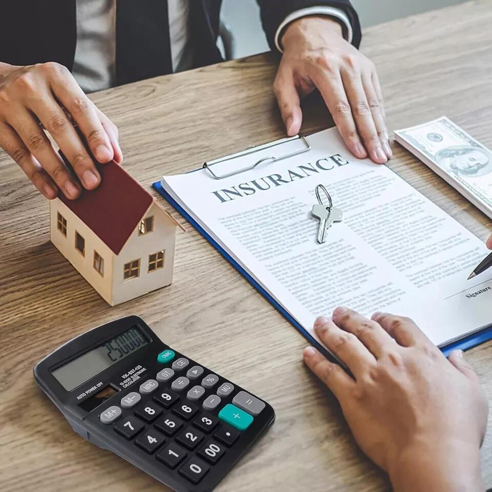 Hands review a home insurance policy beside a house model, keys, cash, and calculator.