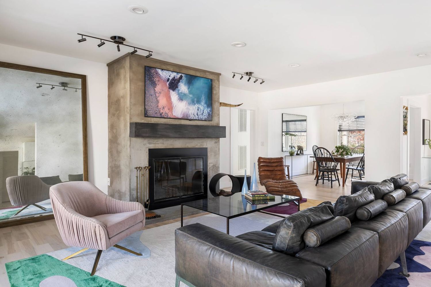 Living room with a concrete fireplace, leather sectional, pink accent chair, and dining area.