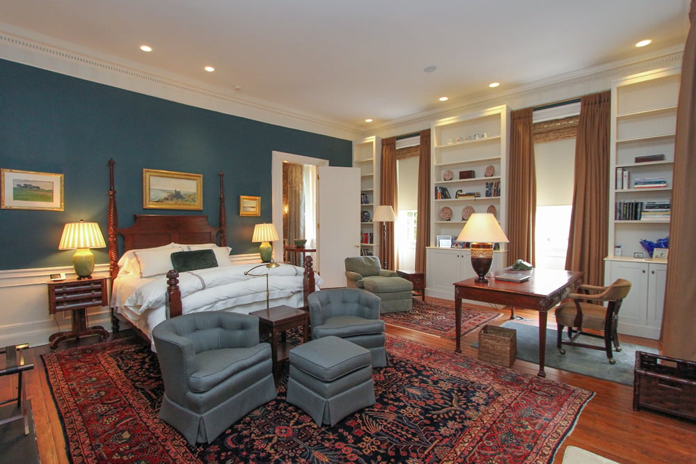 Master bedroom with a four-poster bed, teal accent wall, built-in bookshelves, and patterned rugs.