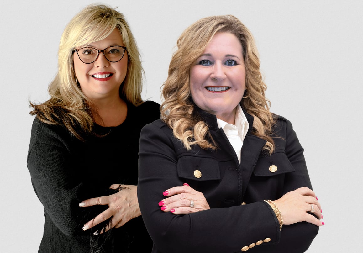 Two smiling women in dark jackets pose with their arms crossed.