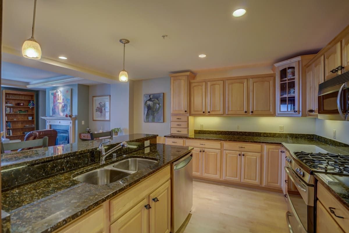 Kitchen with light wood cabinetry, dark granite counters, a double-basin sink, and stainless steel appliances.