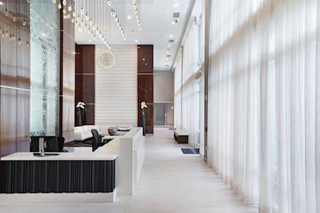 Modern lobby with a long reception desk, white seating, and tall sheer curtains.