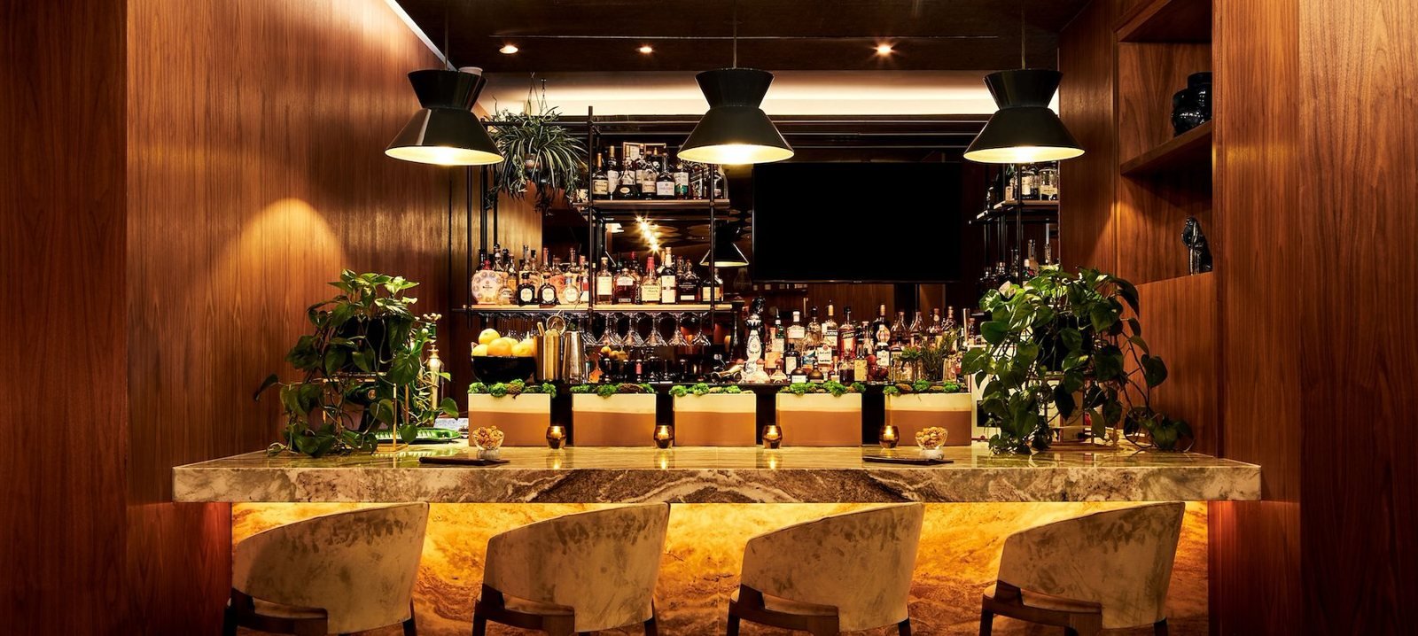 The wood-paneled bar at reveal, with pendant lights over a glowing stone bar top and upholstered stools.