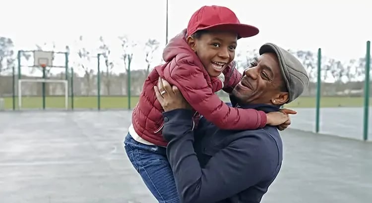 A joyful moment between a man and a child, with the man lifting the child in the air. Both are smiling, indicating a happy family interaction.