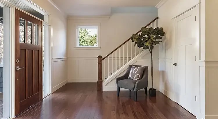 A bright and spacious entryway or hallway of a house, with wooden floors, white walls, and a staircase leading upstairs.