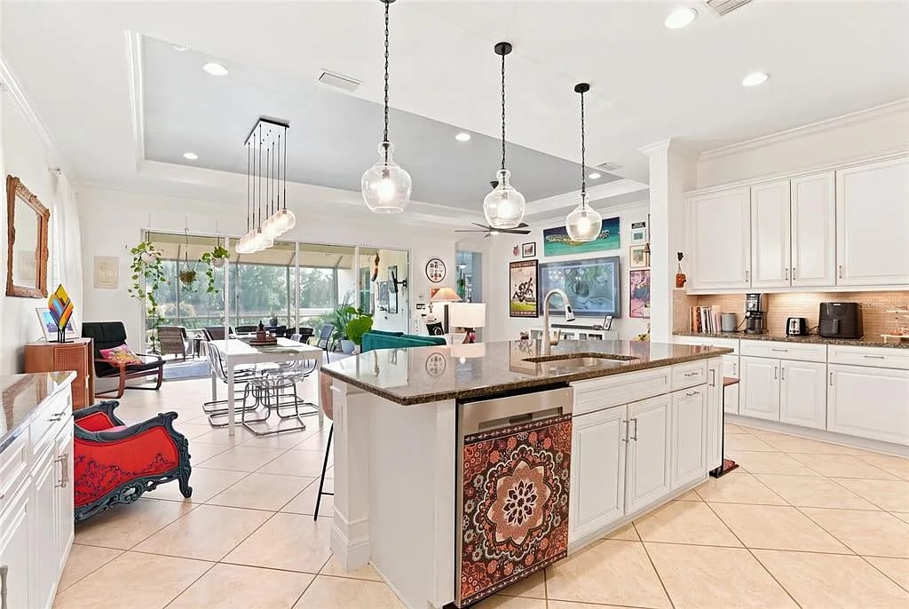 Bright kitchen with a granite-topped island, white cabinetry, and adjoining dining and living areas.