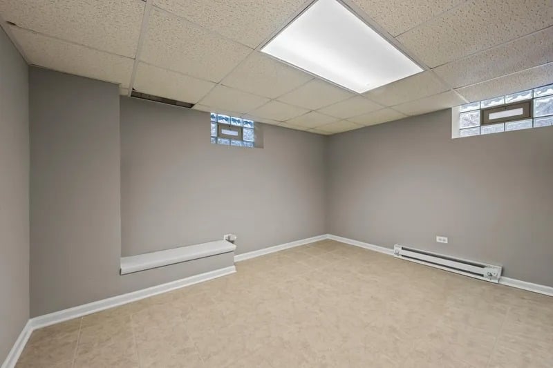 Empty room with gray walls, beige tile flooring, high windows, and baseboard heating.