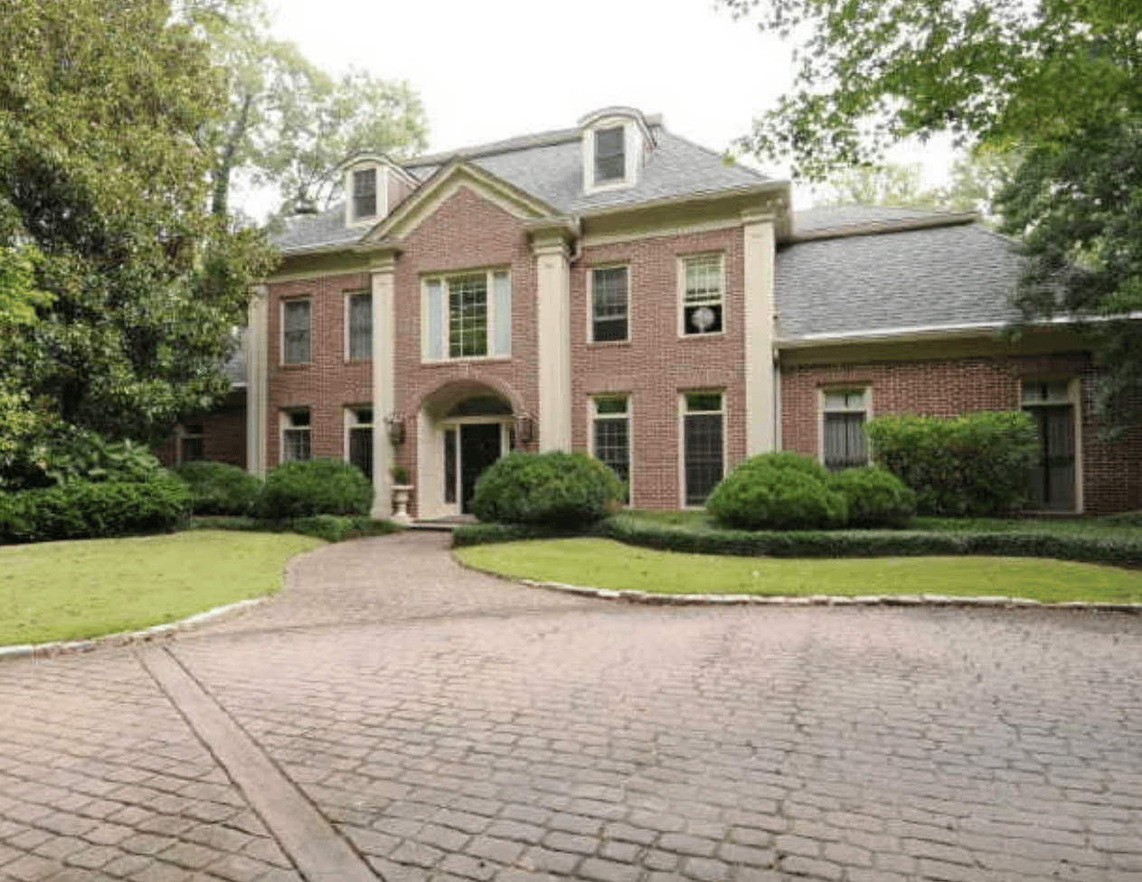 Two-story brick house with dormer windows, an arched entrance, and a curved cobblestone driveway.