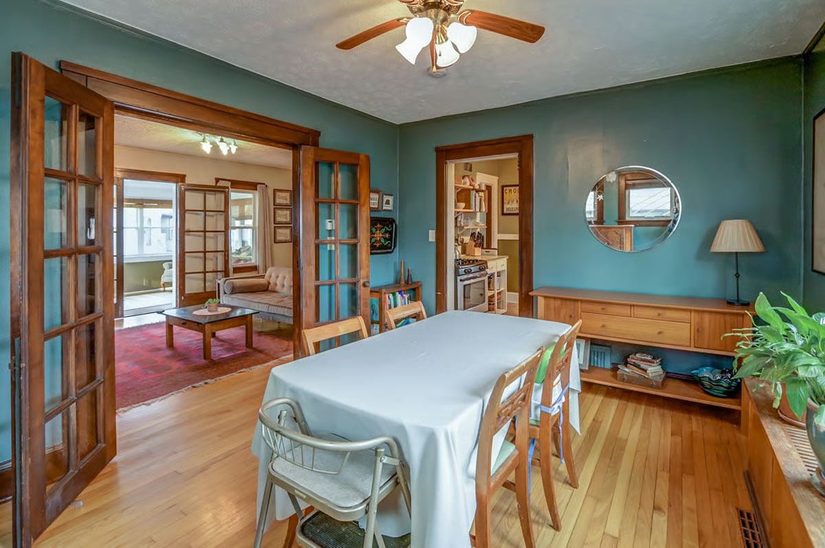 Dining room with teal walls, hardwood floors, and glass-paneled doors opening to a living room.