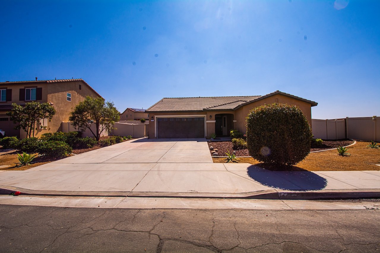 Single-story tan house with a tiled roof, attached garage, wide driveway, and fenced yard.