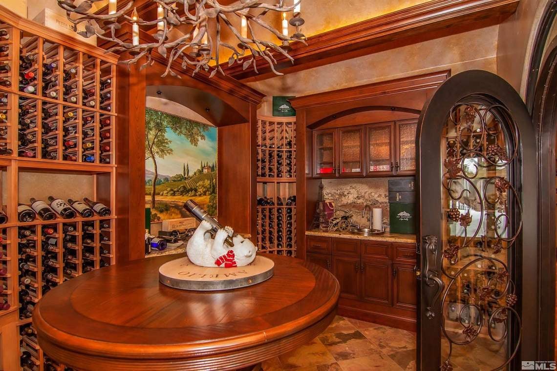 Wine cellar with wooden wine racks, a round tasting table, and an ornate iron-and-glass door.
