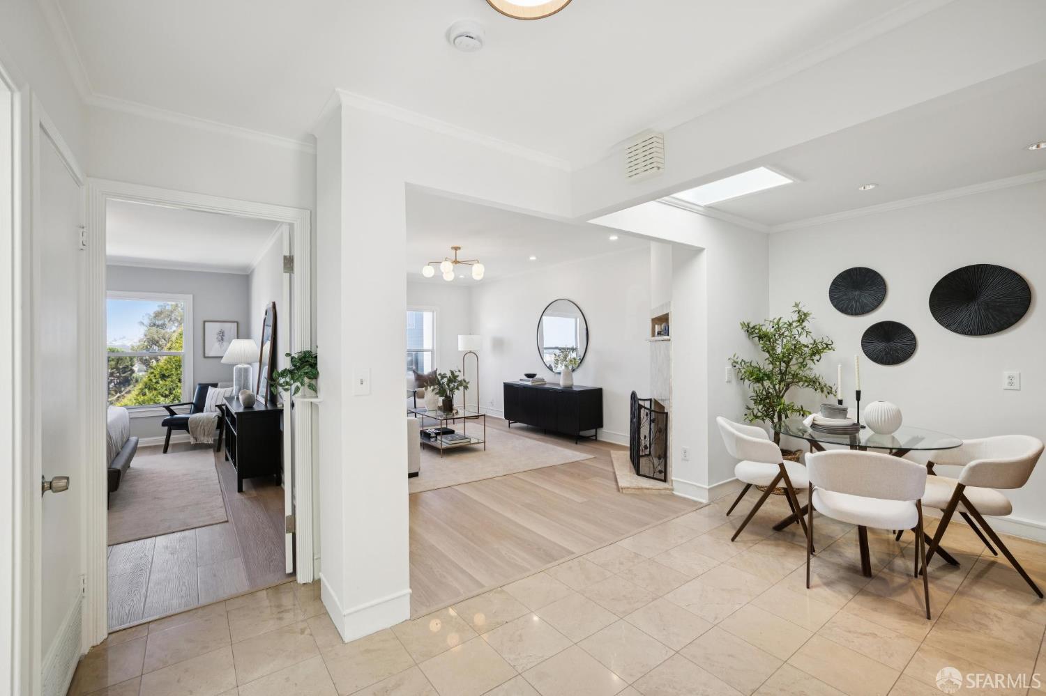 Open-plan dining and living area with a glass table, white chairs, and black circular wall art.