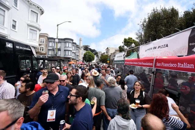 A bustling festival scene in North Beach with families and food lovers sampling pizza slices at various vendor booths, with the San Francisco Italian Athletic Club building visible in the background