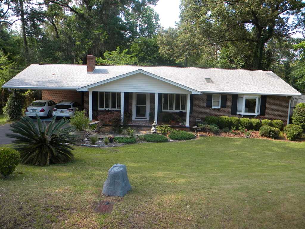 A brick home surrounded by a spacious yard and tall trees, showcasing a serene and inviting outdoor environment.