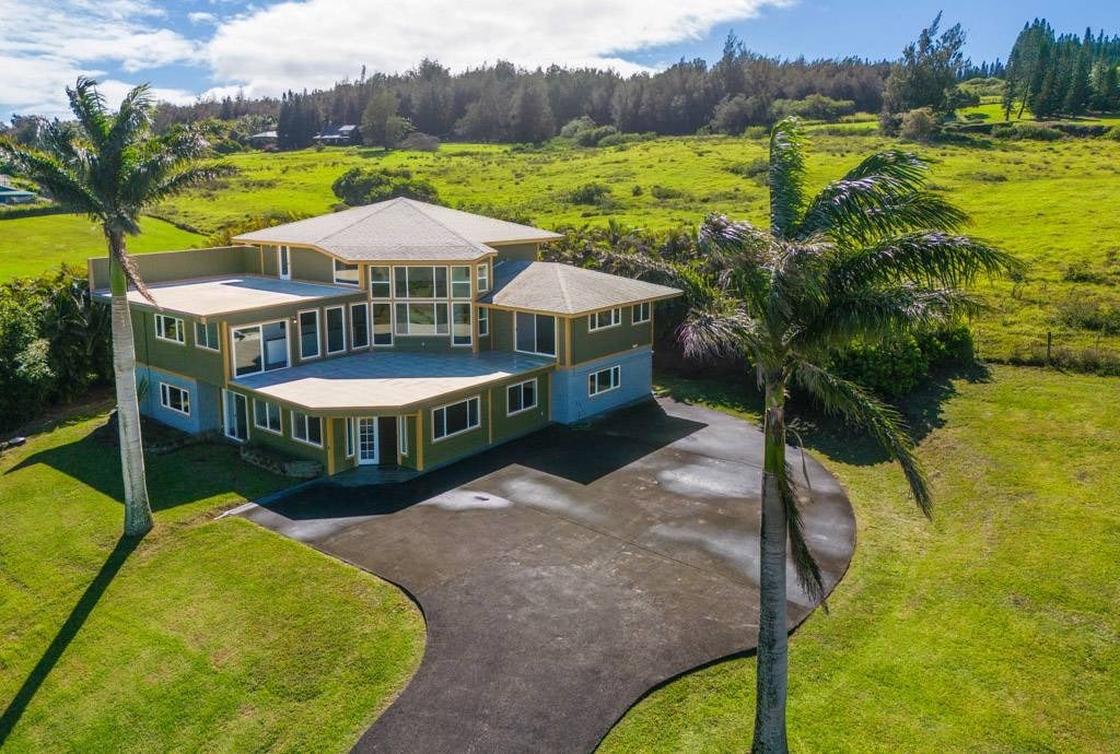 Aerial view of a two-story home with a curved driveway and palm trees amid rolling green grounds.
