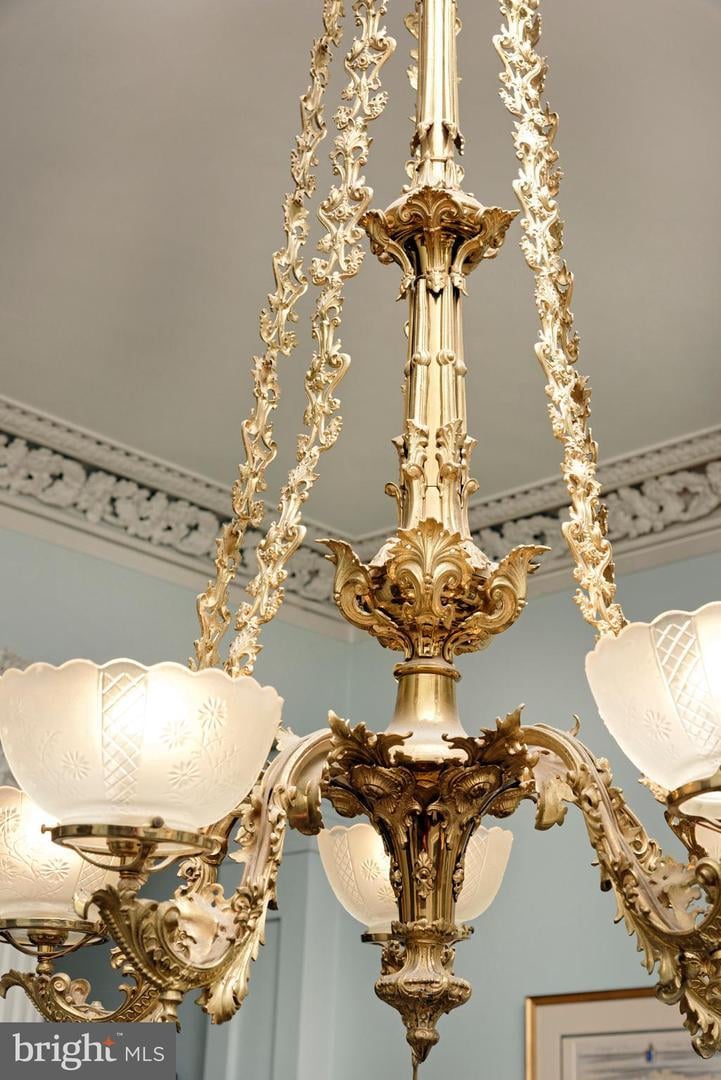 Ornate gold chandelier with frosted glass shades beneath decorative ceiling molding.