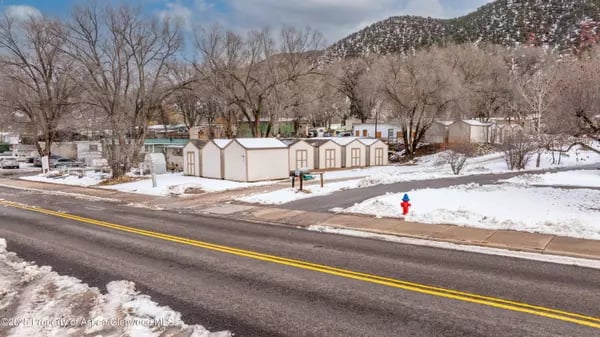 Snowy neighborhood street with detached garages, leafless trees, and a mountain in the background.