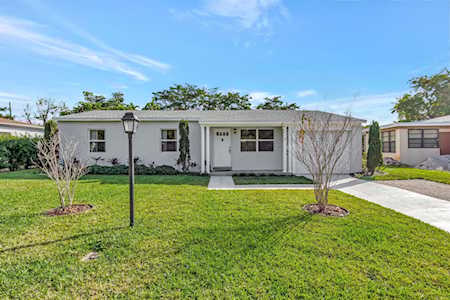 Single-story white home with a broad green lawn, two small trees, and a walkway to the front door.