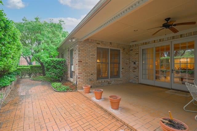 Covered brick patio with a ceiling fan, glass doors, potted plants, and a brick-paved walkway.