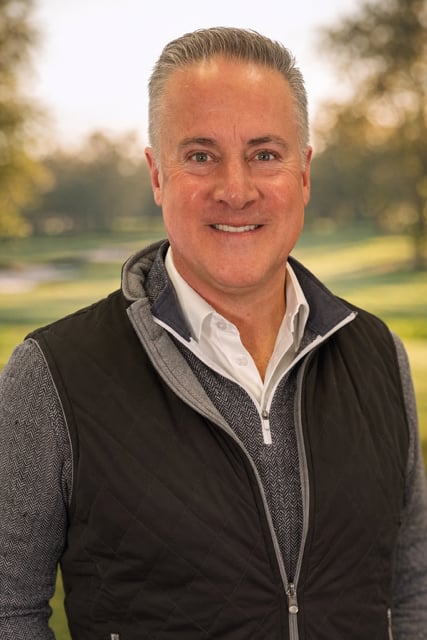 Gary Gardiner, Jr. smiling outdoors in a dark vest and gray sweater.