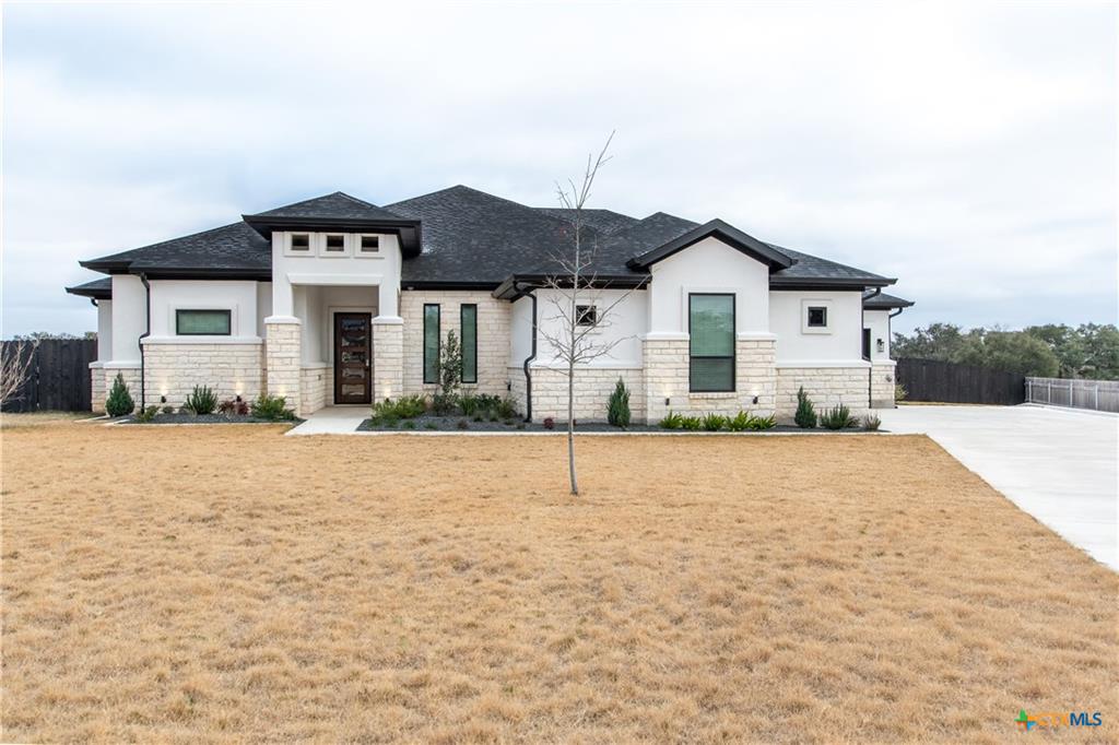 Modern white and stone home with dark roofs, a broad lawn, and a side driveway.