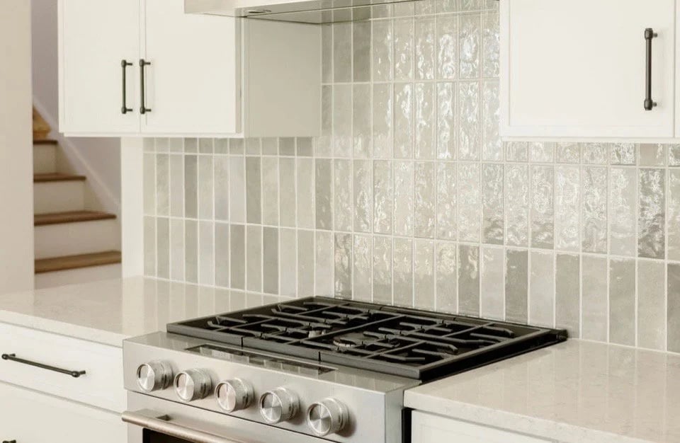 Kitchen gas cooktop with stainless-steel controls, white cabinets, and a patterned tile backsplash.