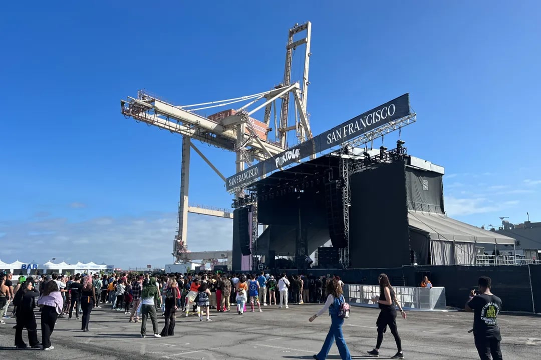 The main stage at the Portola Music Festival at Pier 80 in San Francisco. A large crowd of people gathers in front of the stage, which is set up beneath a massive container crane.
