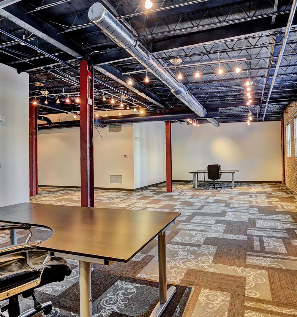 Open office with patterned carpet, red steel columns, exposed ceiling beams, and desks.