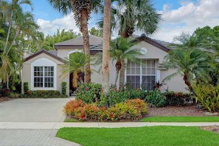 Single-story home with a paved driveway, mature palms, and colorful tropical landscaping.