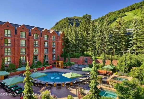 Red-brick condominium building overlooking a swimming pool, surrounded by green mountain slopes.