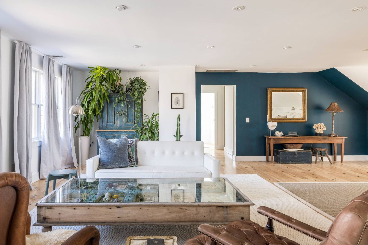 Living room with a white sofa, glass coffee table, leather armchairs, and blue-green accent wall.