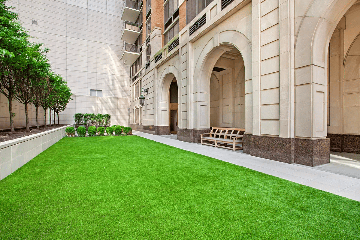 Building courtyard with a broad green lawn, benches, and arched stone entrances.