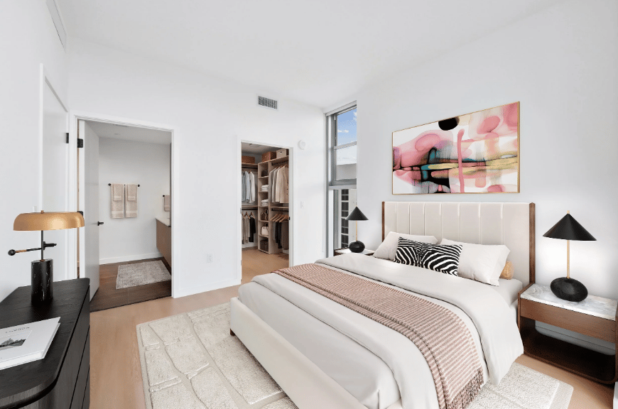 Furnished bedroom with a white bed, colorful abstract artwork, and an open walk-in closet.