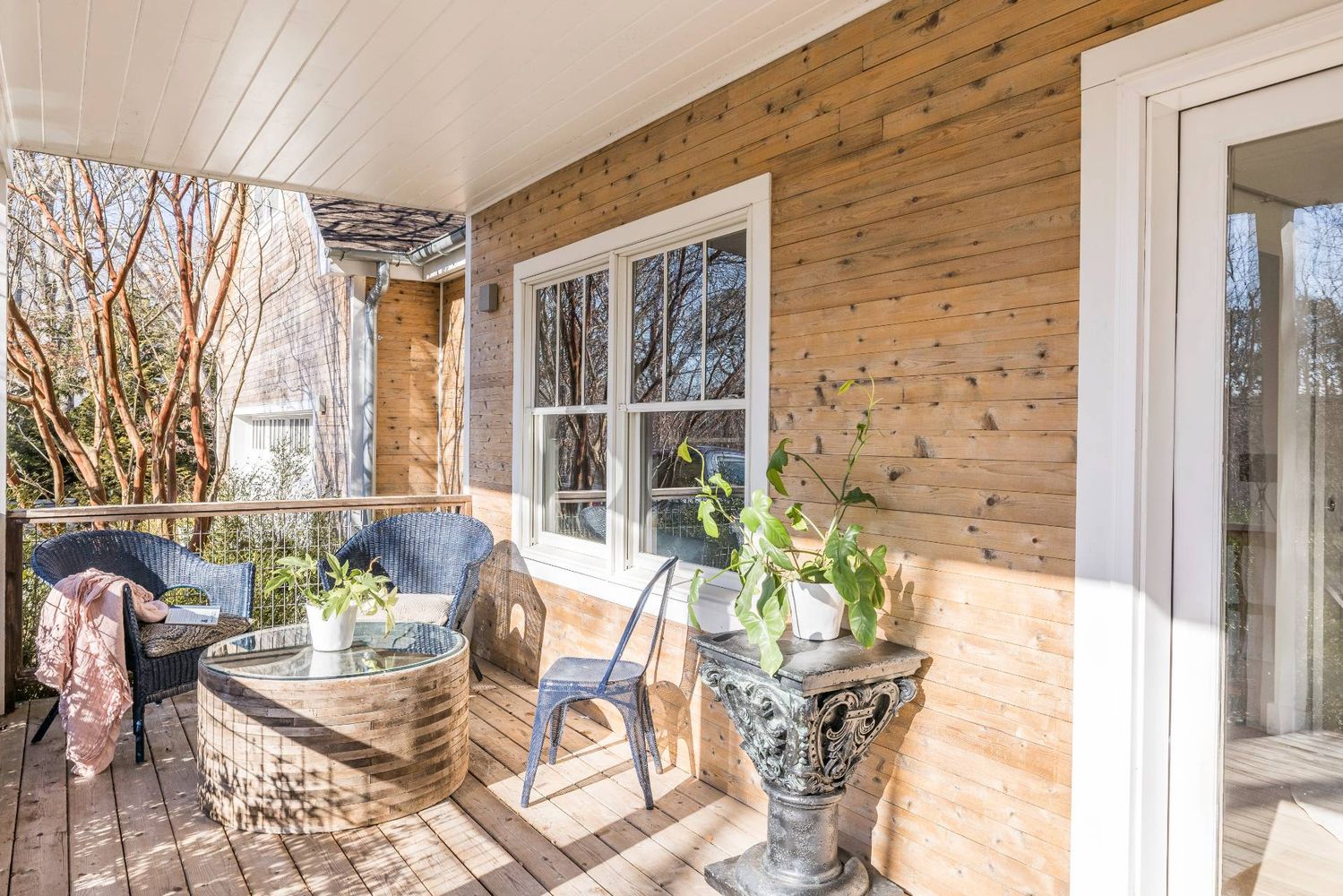 Covered wooden porch with wicker seating, a round table, and potted plants.