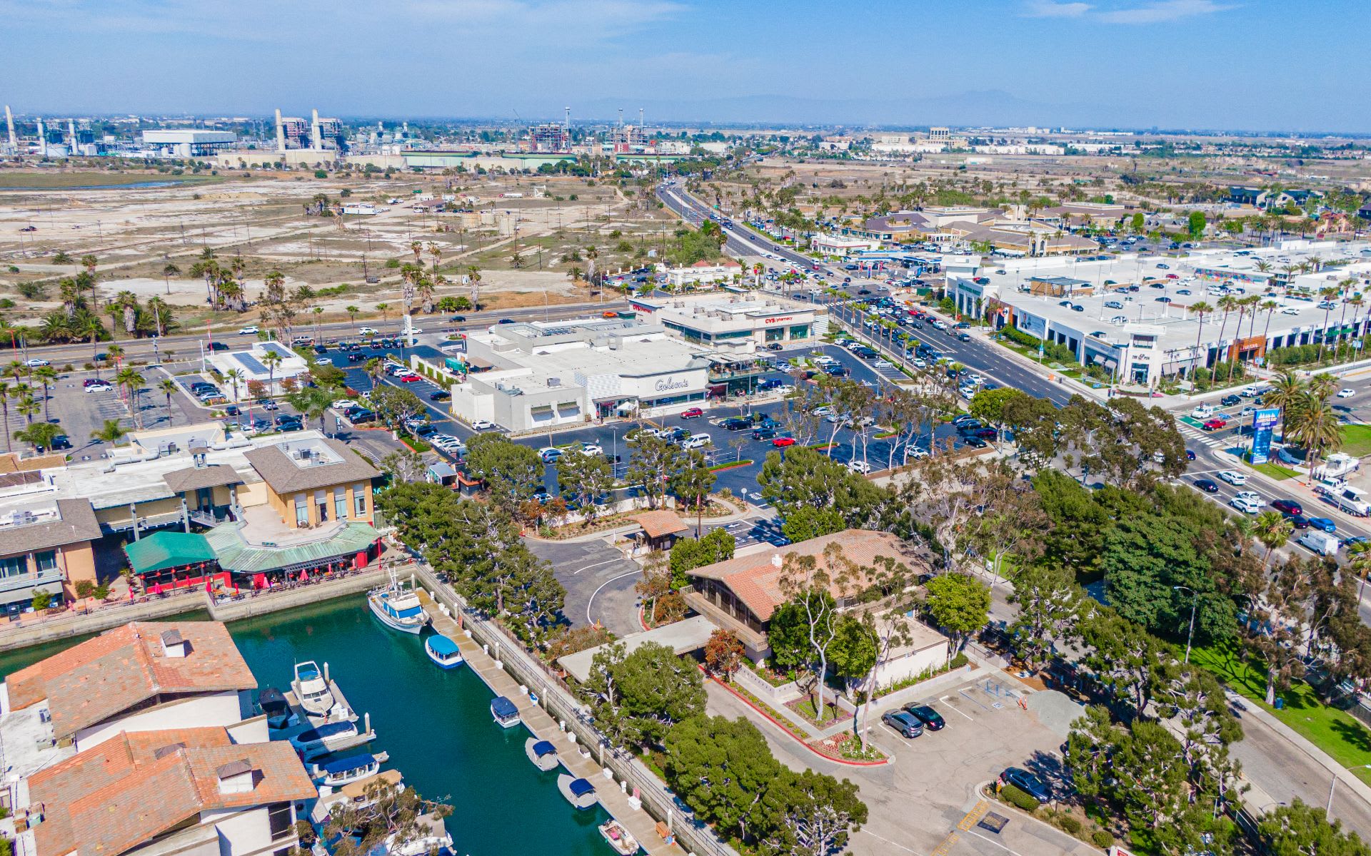 Aerial view of a marina canal with boats beside shopping centers, parking lots, and busy roads.