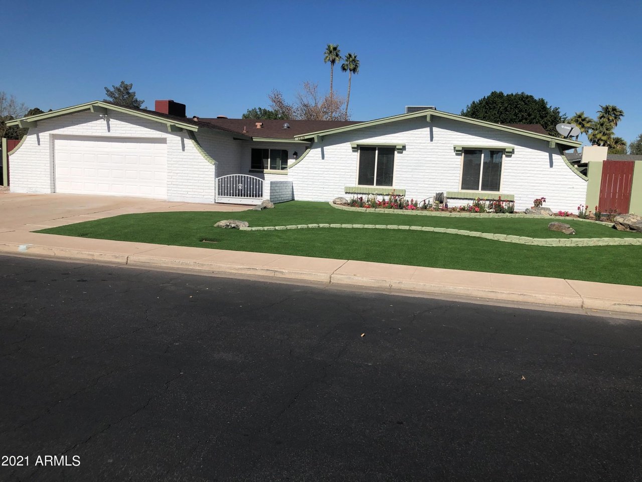 Single-story white brick house with pale green trim, attached garage, and curved front lawn.