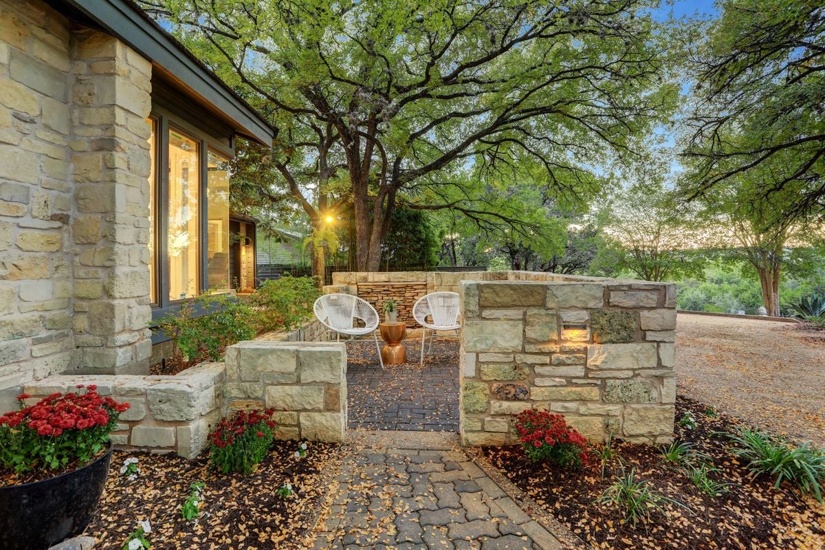 Side-garden stone patio seating nook at 2131 Barton Hills Drive, Austin, TX 78704, framed by mature oak trees. Barton Hills neighborhood.