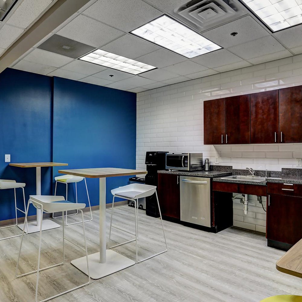 Kitchenette with dark wood cabinets, stainless-steel dishwasher, and high tables with white chairs.