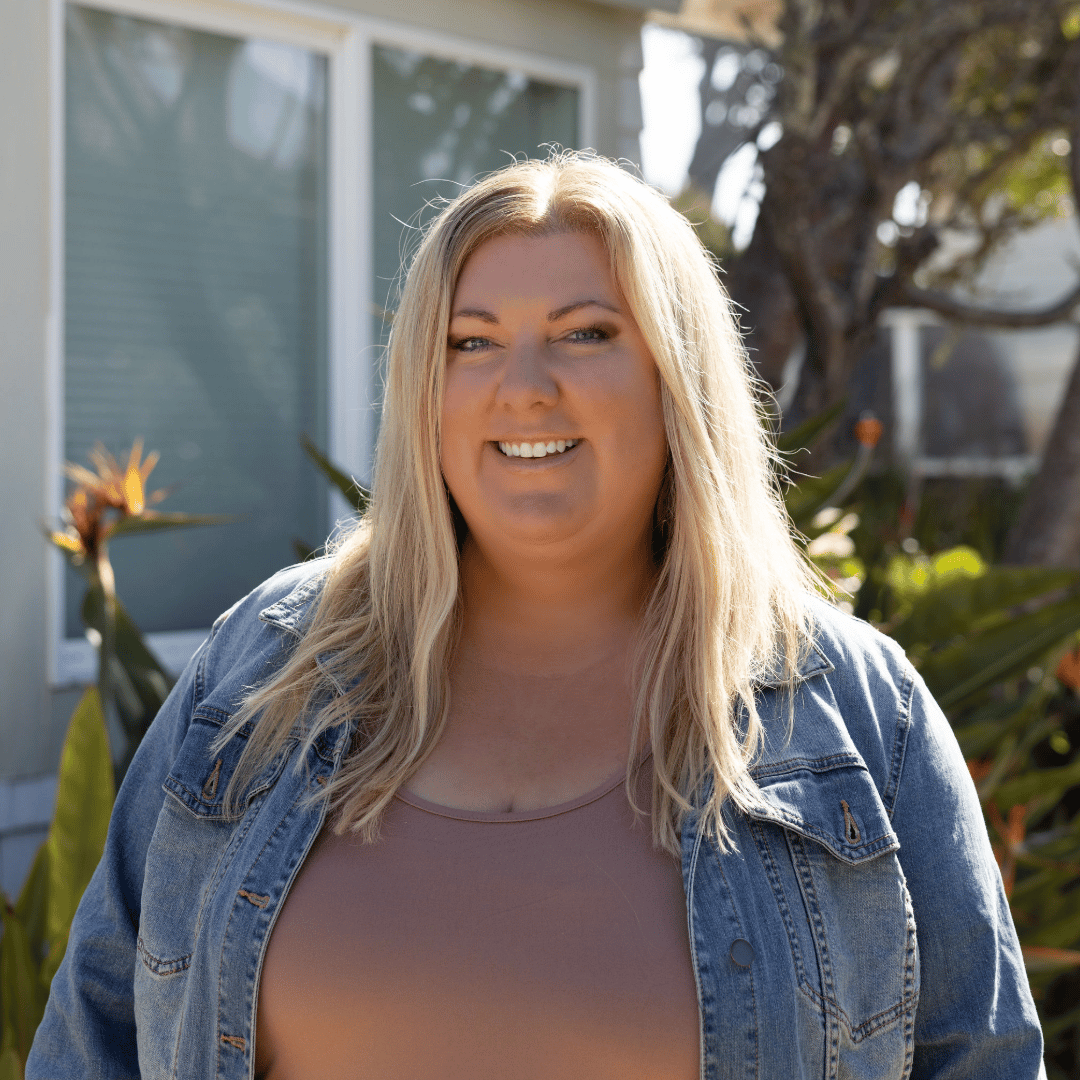 Professional headshot of Alicia Weisbarth, Realtor® and home design specialist at Ocean Element Real Estate, standing in front of a coastal home in Montara, CA.